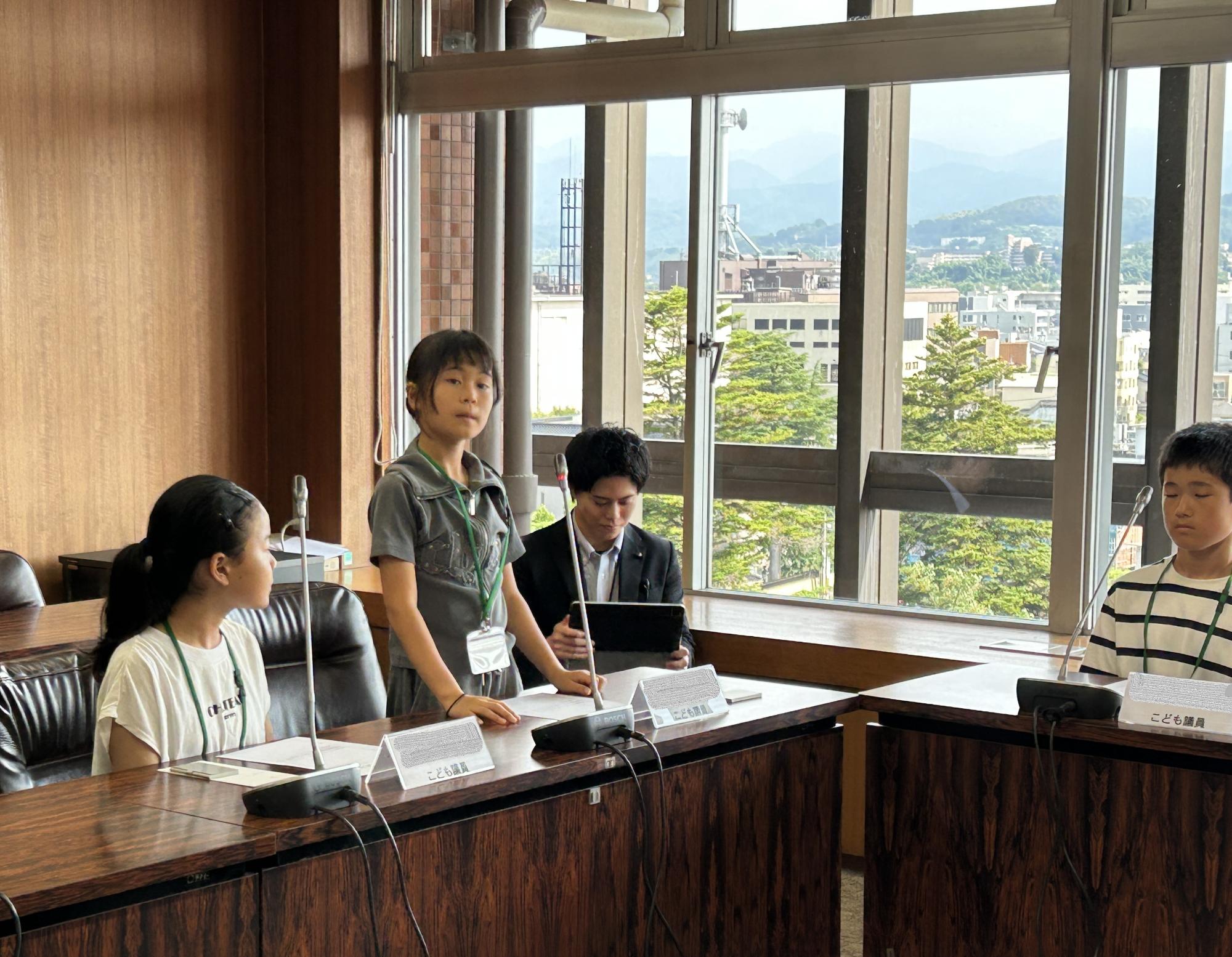 会議室にコの字に設置された長机の椅子に座っている子供たちが議員体験を行っている様子の写真