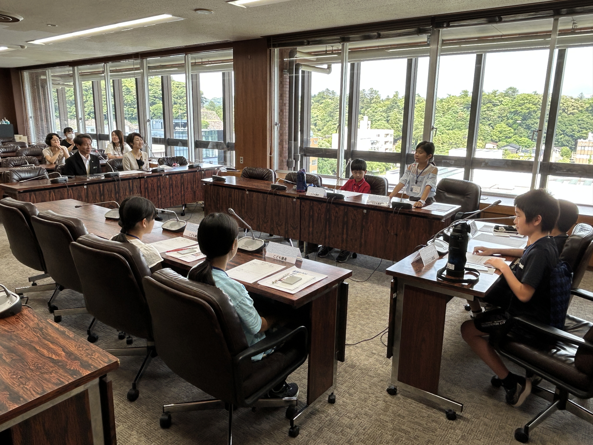 会議室にコの字に設置された長机の椅子に座っている子供たちが議員体験を行っている様子の写真