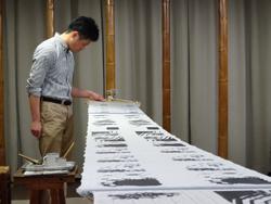 男性が、机の上に並べられた白黒の染画の前に立ってみている写真