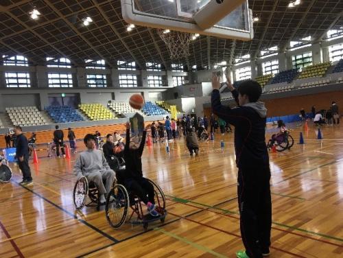 体育館の中で参加している方が車椅子に乗ってバスケットゴールに向かってボールを投げている写真