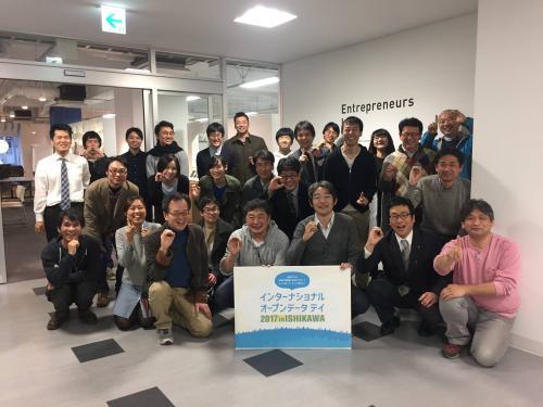 インターナショナルオープンデータデイ 2017 in ISHIKAWAと書かれたパネルを持った男性を中心に参加者が集まり、笑顔で集合写真を撮っている写真