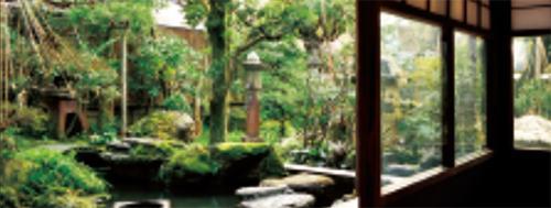 灯籠、庭石、盆栽、緑に色づいた樹木などがある日本庭園の写真
