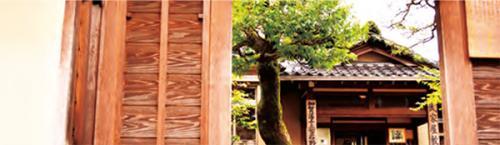 手前の木製の門から撮影した、左奥に樹木と瓦屋根の武家屋敷跡野村家の建物外観写真