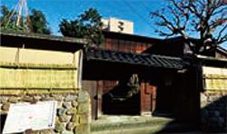 クリーム色の外壁に囲まれた立派な日本家屋の門構えの写真