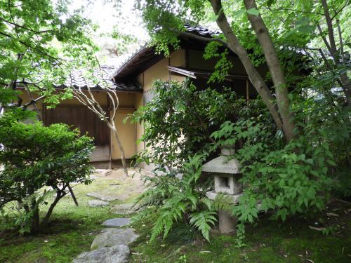 樹木の生い茂った庭園に石灯篭があり、奥にベージュ色の平屋建てが見えている茶室梅庵の外観写真