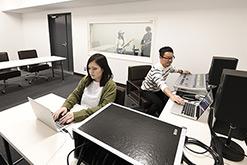 ミキサールームでパソコン操作している女性と音響の機械操作をしている男性の写真