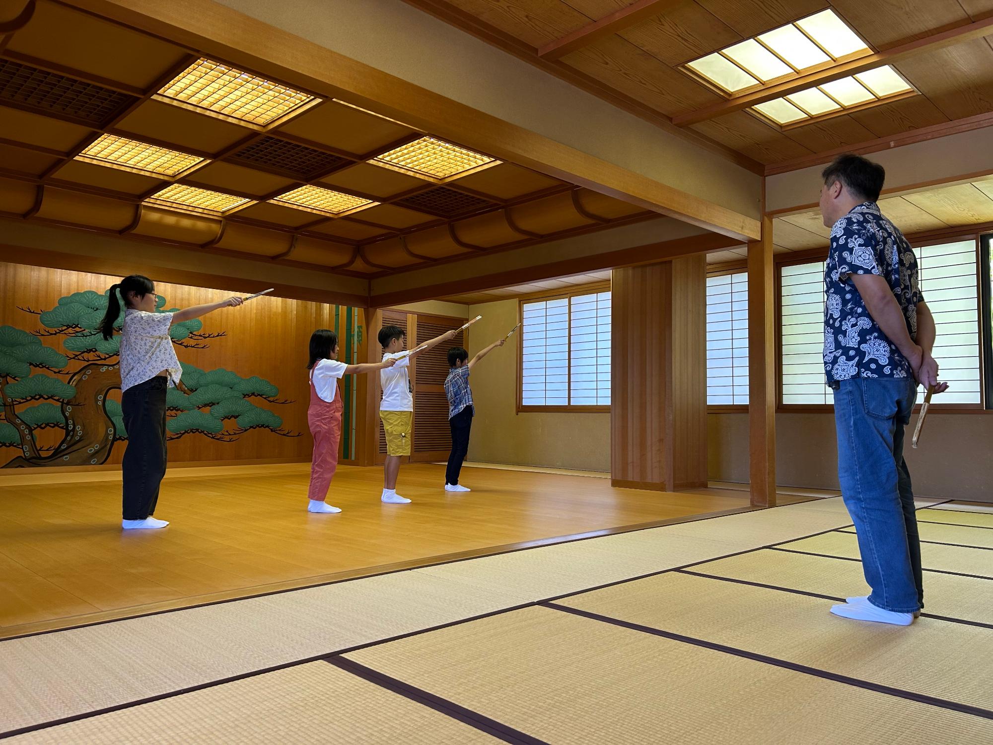 足袋を履き右手に扇子を持った子供たちが先生の前で小舞の稽古をしている写真