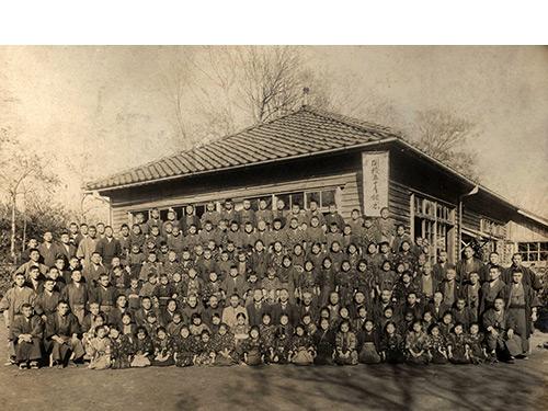 木造の俵小学校校舎前で児童や先生たちが一斉に記念撮影をしている白黒写真