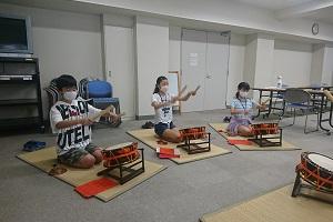 一人ずつ畳マットに座り、両手にバチを持ち太鼓の練習をしている子供たちの写真