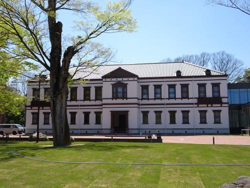 芝生が広がり木が1本立っている後方に、白い壁の洋風2階建ての旧陸軍第九師団司令部庁舎が建っている写真