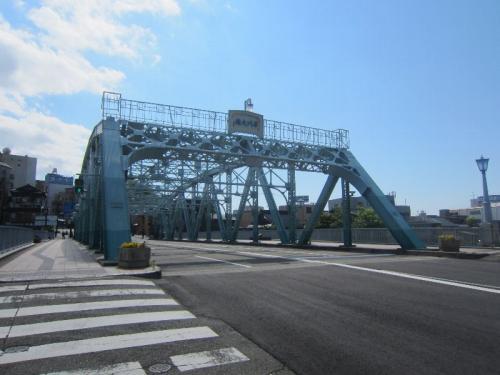 横断歩道の先に、水色の網状になった犀川大橋がかかっている写真