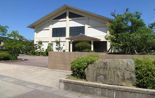 「金沢市埋蔵文化財センター」と書かれた大きな石看板が門の横に設置され、敷地内には庭木が植えられ、白壁で大きな建物の埋蔵文化財センター外観写真