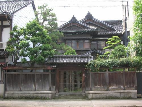 門の後ろに、松の木と桟瓦葺の木造2階建ての趣のある木村家住宅主屋を正面から写した写真