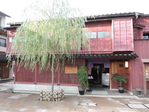前に1本の木が立ち、2階建て、レンガ色に染まるベンガラを塗った出格子の旧諸江屋の写真