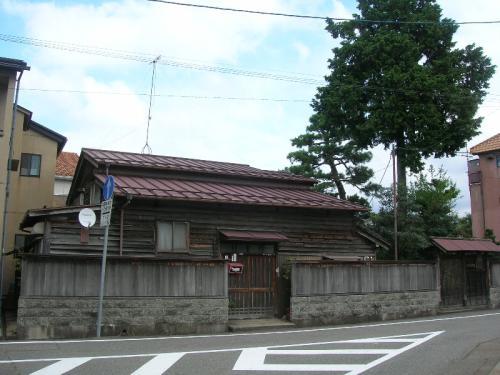 コンクリートの塀で囲まれ、赤い屋根がついた木造の建物が写っている平木家住宅主屋の外観写真