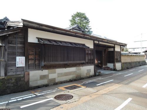 敷地を囲む土塀から連なる、亜鉛鉄板葺きの緩い屋根造りの長屋門を道路の反対側から撮影した、野坂邸の写真