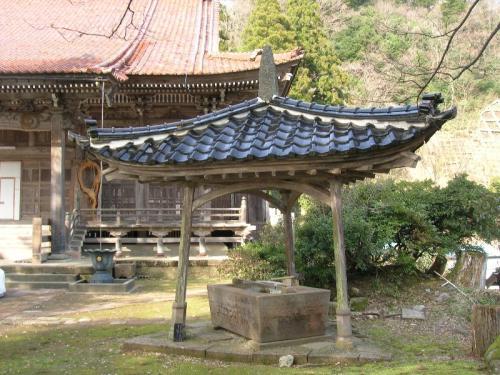お寺の本堂前に立つ瓦屋根のついた手水舎が写っている本泉寺手水舎の外観写真
