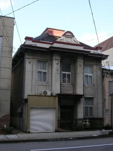 木造2階建て、瓦屋根、4本の角柱の形を浮彫りにしてある上野家住宅旧診療所の写真