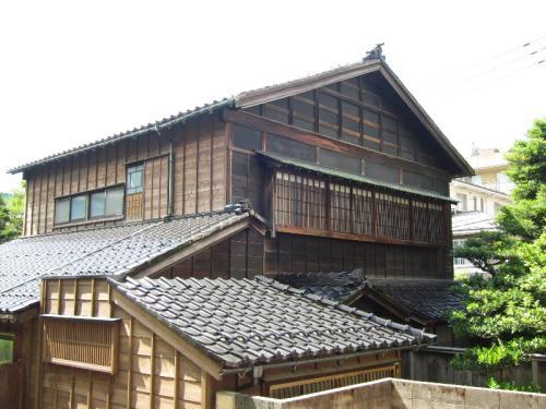 木造2階建て、2階は格子の窓がある、昔ながらの切妻屋根の旧野村家住宅主屋の写真