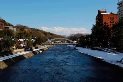 堤防に雪が積もり、流れる川の奥に、アーチ状の天神橋が掛かっている写真