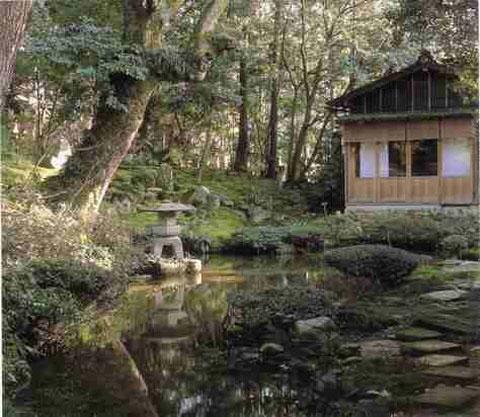 樹木が生い茂った中にある池の奥に建つ建物と石灯篭や敷石がある心蓮社庭園の写真
