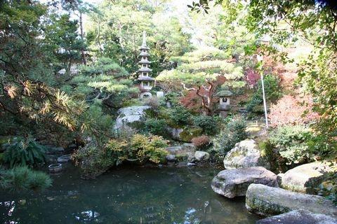 池の周りに庭石や庭木、五重塔の石灯篭などがある西家庭園の写真