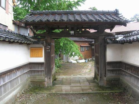 白色の塀に瓦屋根が付いており、塀の先が門になっている妙泰寺山門の正面写真
