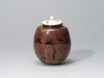 全体的に濃淡のある茶色の陶磁器に白い蓋がついている茶入の写真