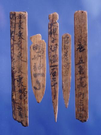 木札に墨で文字が書かれ、一部破損している木簡（もっかん）が5枚並んでいる写真