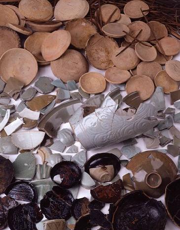 沢山の丸い土師器（はじき）皿や割れてしまったツボ、割れた皿や器の破片が並べられている堅田館跡の出土遺物の写真