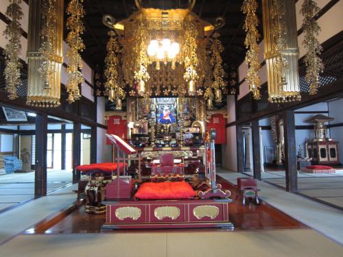 天井から金色の装飾品が下がり、建物内の中央に本尊が祀られている内陣の写真