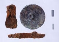 茶色に錆びている鉄製の武具や円形の銅鏡などが並んでいる神谷内古墳群・副葬品の写真