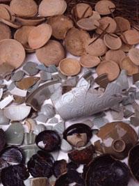 沢山の丸い土師器（はじき）皿や割れてしまったツボ、割れた皿や器の破片が並べられている堅田館跡の出土遺物