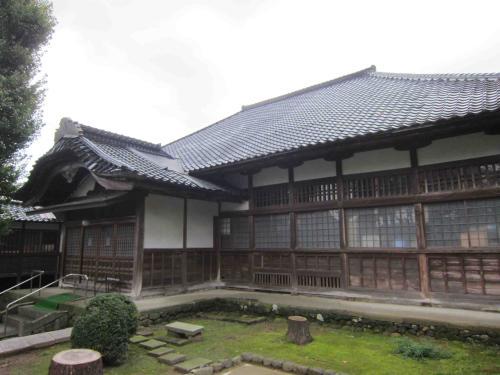 建物前に木を切った後の切り株や敷石のある庭がある、木造平屋の松山寺本堂外観写真