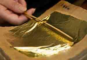 箔打紙の上に乗せられた金箔を2本の棒で挟むように持ち上げる作業をしている写真