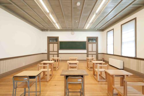 黒板の両脇に縦長の棚が置いてあり、机と椅子が9組並べられている旧石川県第二中学校本館講座室内の写真