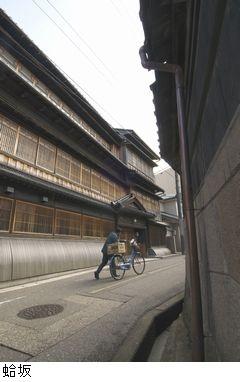 家と家の間にある細い道路を自転車を押しながら登る人が写っている蛤坂の写真