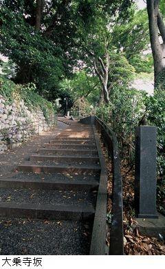 右側に木が立っていて、左側は石垣、中央には奥まで続く長い階段のある大乗寺坂の写真