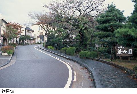 手前に兼六園の看板、右側には木が並び、中央にはS字カーブの道が続いている紺屋坂の写真