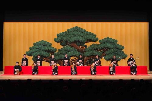 大きな松の木が描かれた屏風の飾られた舞台で小鼓、大皷、笛、三味線を演奏する和服姿の女性たちの写真
