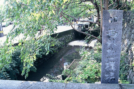手前右側に「西外惣構堀」と記された石碑が設置された下に川が流れている写真