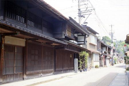奥まで真っすぐに続く通りの左側に、昔ながらの町家様式の建物が軒を連ねている写真