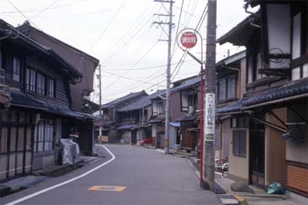 左に曲がった緩やかなカーブの道路の両側に、伝統的な町家建築の建物が軒を連ねている写真