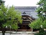 手前両側に樹木があり、奥に寺院の本堂がある写真