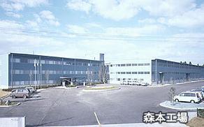 駐車場に数台駐車され、3階建ての建物の澁谷工業株式会社 森本工場の外観写真