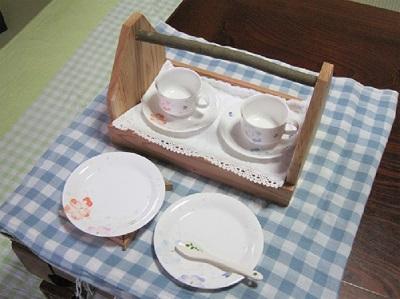 木製のおかもちの上に置かれた2組のティーカップと、その前に並べられたお皿2枚の写真