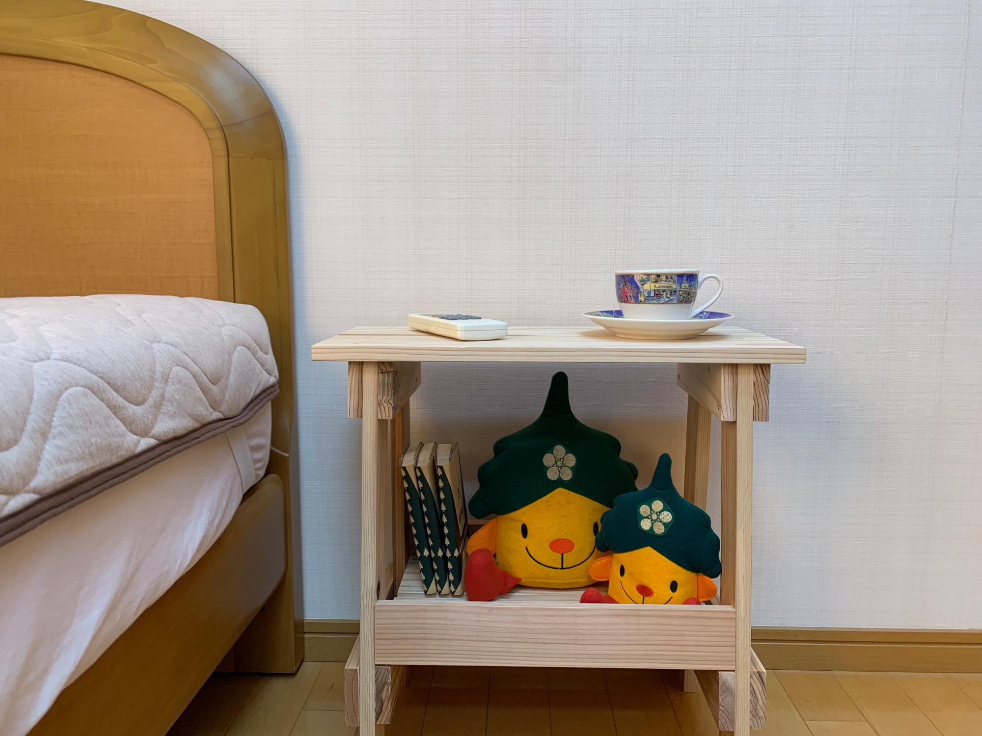 ベッドの脇に置かれているサイドテーブル。かなりんのぬいぐるみや本が下段に収納されており、上段にリモコンとティーカップが置かれている。