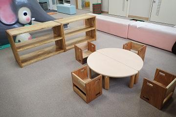 スギ間伐材で作られた子ども用の小さい丸テーブルの周りに同じ木材で作られた4つの椅子が並べられ、背後には本棚が配置されている様子