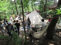 森の中にテントやハンモックが置かれて、参加者達が準備をしている写真