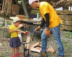 黄色のTシャツを着た男性と子供が向かい合い木を使って作業をしている写真